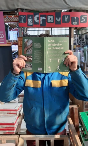 Homme tenant le livre Auto construire en réemploi lors de la visite de L’Écrouvis Recyclerie de matériaux & Éco-construction